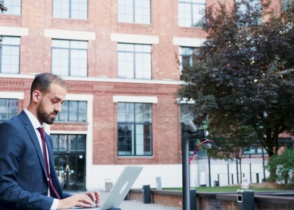 Successful businessman in suit working at marketing presentation sitting on bech outside in front of corporate building office. Executive manager searching information on internet.